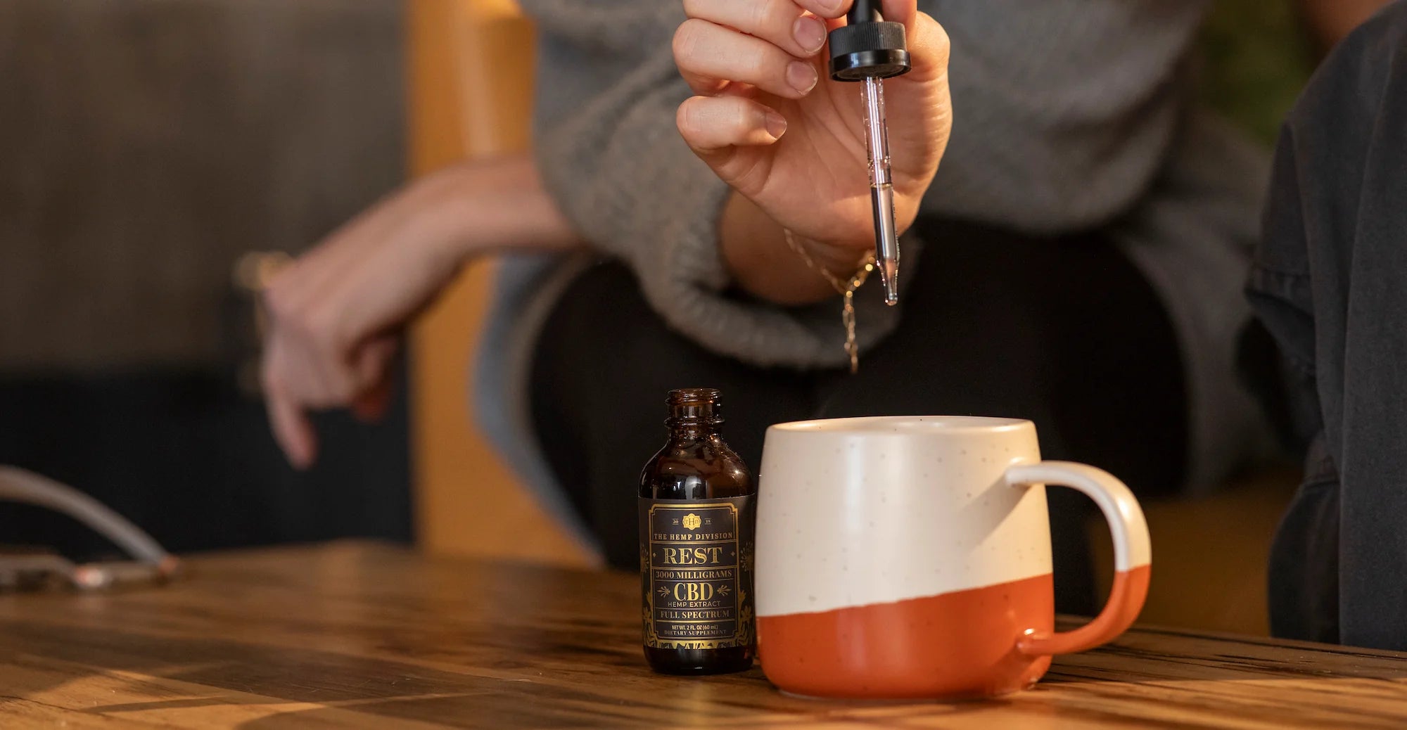 Hand holding a dropper over a mug, with a bottle labeled “REST 3000 Milligrams CBD Hemp Extract Full Spectrum.”